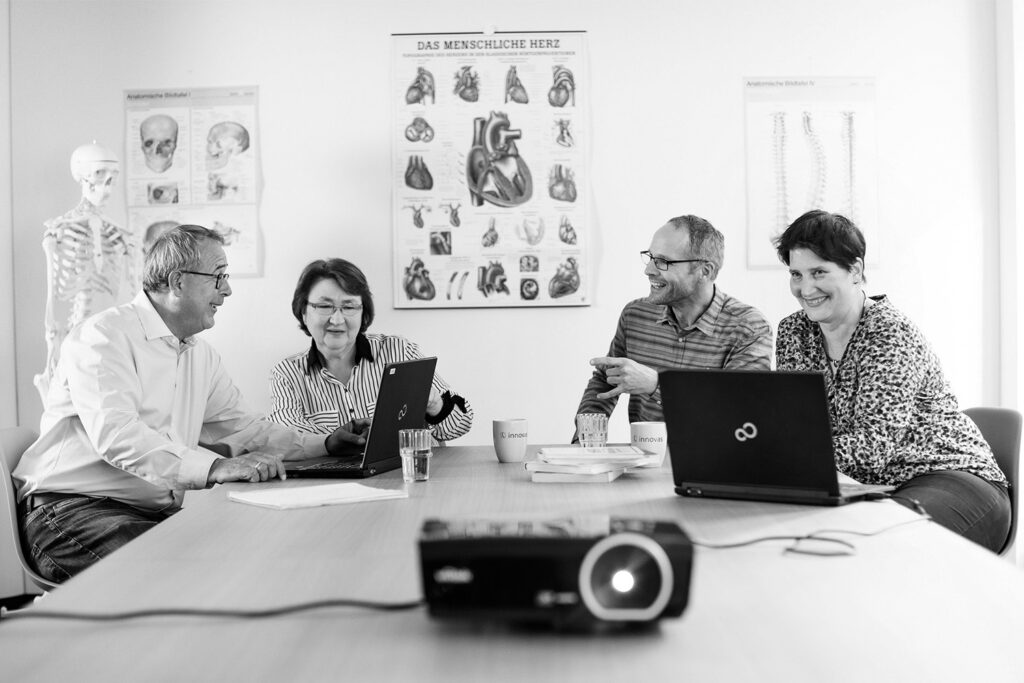Vier innovas-Mitarbeitende in einem Besprechungsraum mit medizinischen Abbildungen